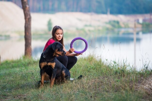 imgi_433_little-beautiful-cute-girl-big-adult-rottweiler-dog-sitting-edge-sandy-cliff-playing-with-dog-toy-ring-enjoying-warm-summer-morning-dense-spruce-forest_212944-